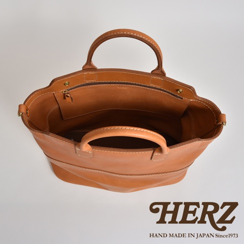 棕色皮革製成的大容量兩用托特包，頂部開口有拉鍊，包身結構柔軟，雙提把設計，縫線清晰。