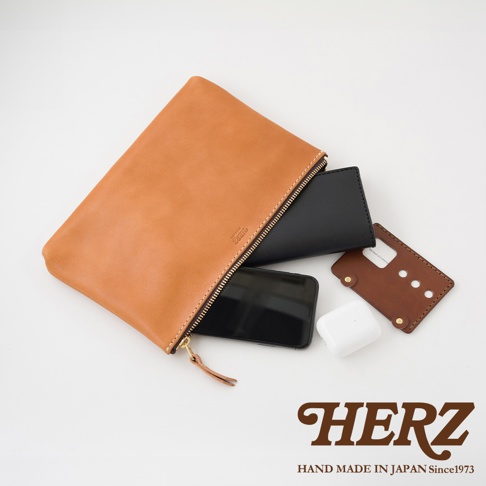 一個打開的淺棕色皮革長方形拉鍊收納包，內含一個黑色手機、一個黑色皮夾和一個白色無線耳機。收納包外側印有品牌標誌。