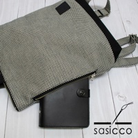 一款黑白格紋刺子織手提後背包，搭配黑色皮革記事本，背包有肩帶可調，材質為織布與皮革。