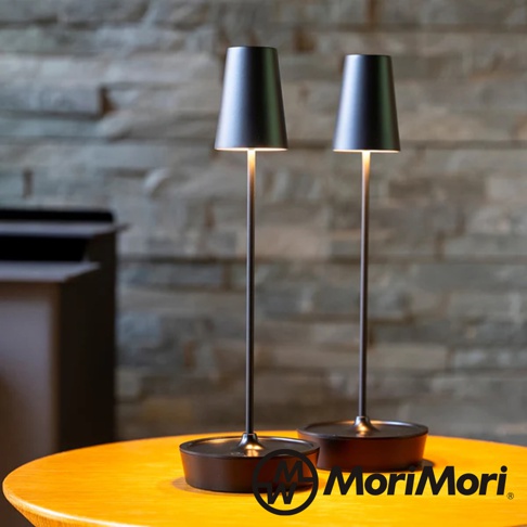 兩盞黑色金屬復古氛圍燈，帶有錐形燈罩和細長燈柱，擺放在木質桌面，背景為石牆。