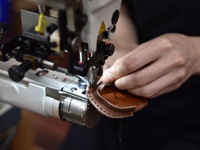 職人使用縫紉機，正在縫製棕色皮革製品。皮革邊緣有明顯的縫線，展現手工製作的細節。