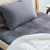 深灰色美麗諾羊毛保暖墊鋪設於單人木製床架上，墊上放置一個深灰色枕頭，下方另有白色羽絨被。