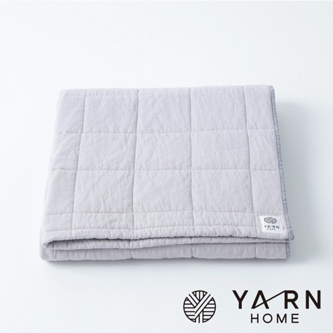 淺灰色格紋鋪棉浴巾，由脫脂棉混紡紗製成，表面有細緻的格紋縫線，左下角有品牌標誌。