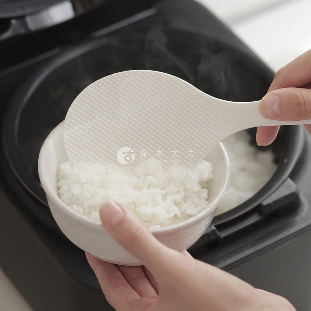 日本marna站立式飯匙正從裝有熱騰騰白米飯的碗中盛飯，飯匙上有防沾壓紋設計，握把為立體造型，方便好握。
