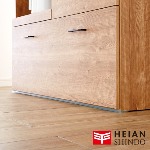 淺色木紋家具底部，裝有黑色長條形把手，下方邊緣處可見一條灰色防倒固定墊，與淺色木地板緊密貼合。