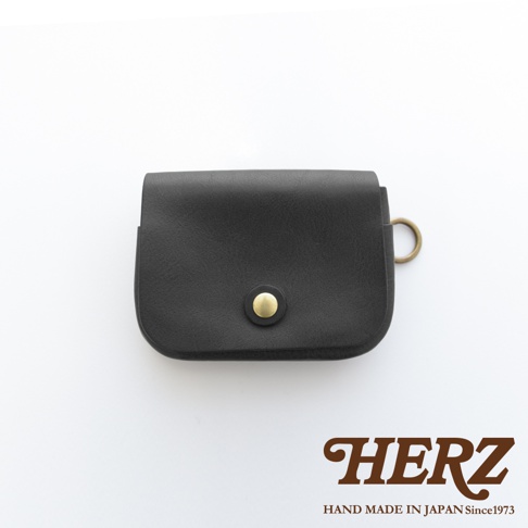 黑色皮革製成的職人手作雙層錢包，正面有金色鈕扣，側邊有金屬 D 型環，適合旅行使用。