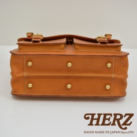 職人手作皮革旅行包 A-102，採用 tan 色皮革，雙層設計，設有兩個前袋，金色金屬扣及鉚釘，車縫線明顯，展現精緻工藝。