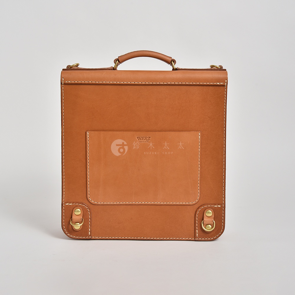 職人手作皮革三口袋三用後背包 A-19-R，呈現天然棕色皮革，具有堅固縫線與金屬扣環。正面有一個方形外袋，袋蓋上印有「HERZ 鈴木太太 SUZUKI SHOP」品牌標誌。