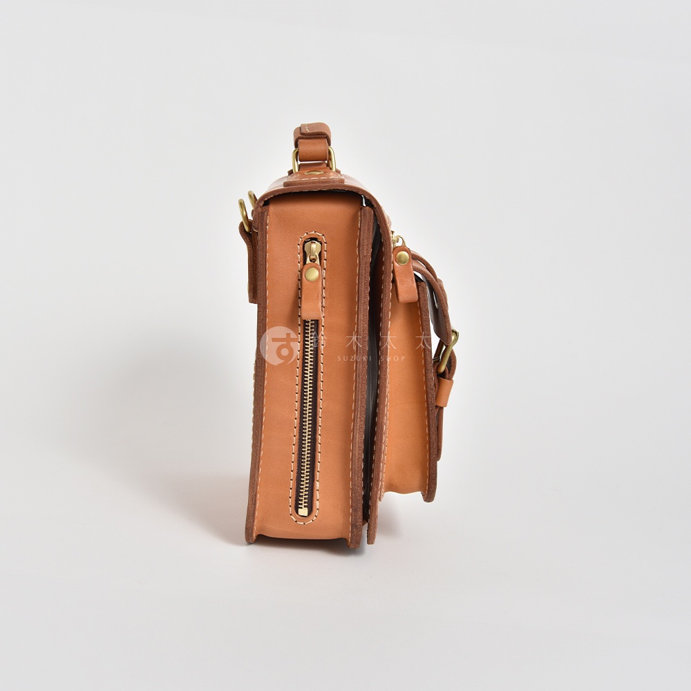 淺棕色職人手作皮革立體口袋兩用單肩包，側面特寫，展示拉鍊、金屬扣環和縫線細節。