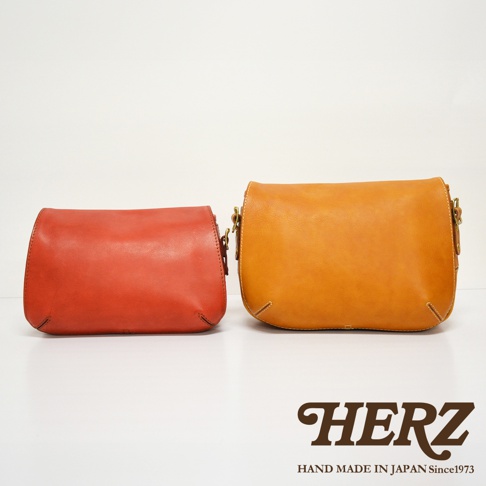 職人手作皮革復古翻蓋郵差包，左側為紅色，右側為棕褐色，兩款包均為柔軟皮革製成，設有金屬扣環和縫線細節，復古設計。