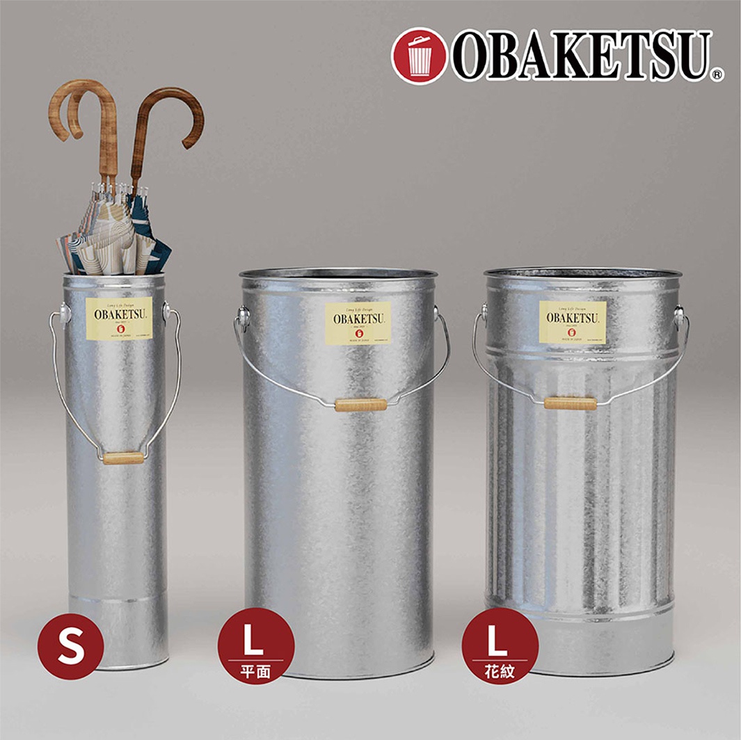 OBAKETSU 品牌標誌旁擺放著三個金屬傘桶，分別為 S 尺寸、L 尺寸平面紋和 L 尺寸花紋，其中 S 尺寸傘桶裡插有雨傘。
