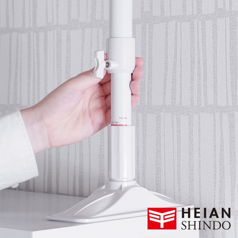 白色伸縮防傾桿，頂部設有可調節旋鈕，底部為寬闊的底座，由塑膠製成，用於支撐和固定。