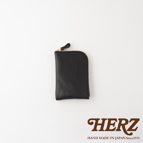 日本HERZ職人手作迷你皮夾，採用黑色Stare皮革製成，呈現簡約直式輪廓，配有金色拉鍊與皮革拉環，右側邊緣帶有圓弧設計，整體為手工縫製質感。