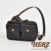 黑色皮革雙口袋斜背包，正面有兩個帶有金色鈕扣的翻蓋口袋，主袋採用金色拉鍊開合，配有可調節的皮革肩帶，整體風格簡約實用。