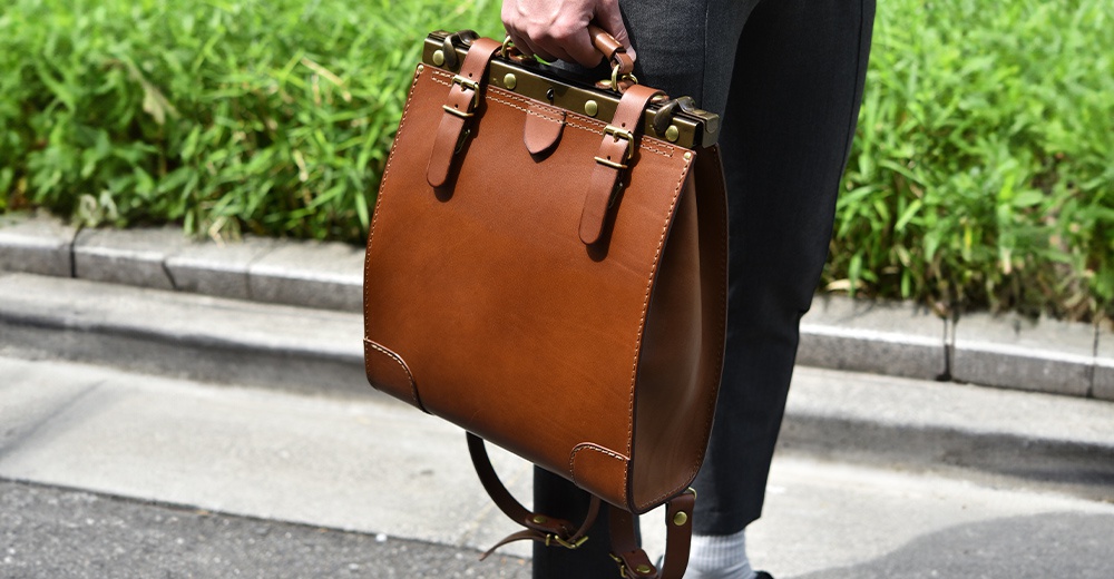 職人手作皮革復古口金後背包，採用堅固的棕色皮革製成，配有黃銅色金屬口金、可調節皮帶和雙搭扣設計，適合日常攜帶。