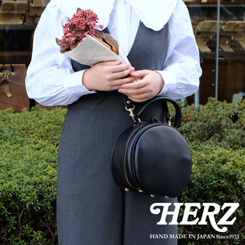 HERZ 品牌手作圓形皮革斜背包，附有品牌標誌 HAND MADE IN JAPAN Since1973。