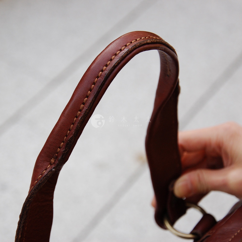 職人手作皮革迷你波士頓包，深棕色水洗皮革材質，手提帶有精緻縫線細節，一端連接金色金屬環。