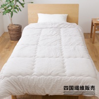 一張鋪設在單人床上的舒芙蕾透氣四季被（中棉款）。被子呈純白色，表面有細緻的壓紋，呈現格紋縫合。床鋪背景為淺木色床頭板和木質地板。