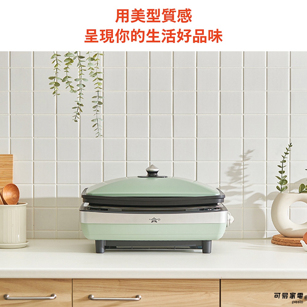 淺綠色遠紅外線石墨烤盤，帶有銀色鍋蓋和把手，放置於白色檯面上，背景為白色格紋牆壁。