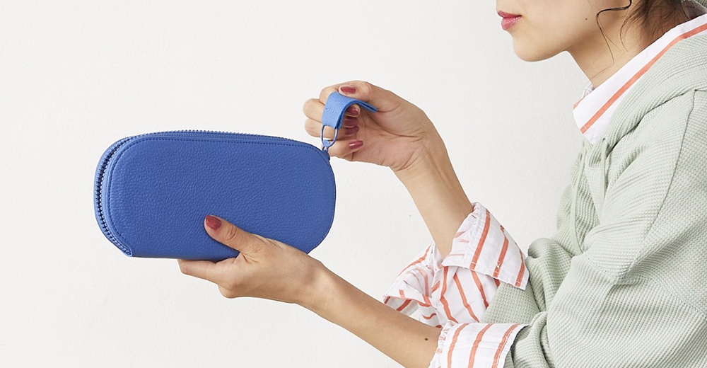 一位女性手持著一個藍色的皮夾，她穿著一件綠色的連帽外套和條紋襯衫。