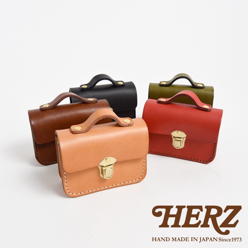 職人手作皮革迷你收納包，展示多種顏色（包括棕色、黑色、紅色、綠色和橘色），採用真皮材質，配有金色金屬扣環和提把，風格簡約。