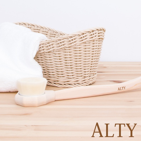 淺色木柄的長柄沐浴刷，刷頭為米白色細軟毛。旁邊擺放著一條白色毛巾和一個米色編織籃。