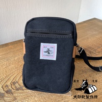 黑色石洗帆布斜背手機包，附有白色方形標籤，上面印有日文圖案。包包設有拉鍊開口及肩帶。