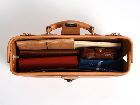 職人手作皮革橫長形杜勒斯單肩包 (CW-4)，淺棕色牛皮製成，頂部有提把和金屬扣，包內裝有書籍、皮夾、藍色印花布和一個小皮製收納包。