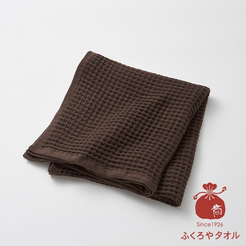 深棕色格子紋理的毛巾，一角疊起，呈現柔軟質感