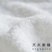 近距離特寫白色蓬鬆柔軟的匹馬棉毛巾，可見細緻的織紋和羽翼般的紋理，底部右側有「天衣無縫 organics」字樣。