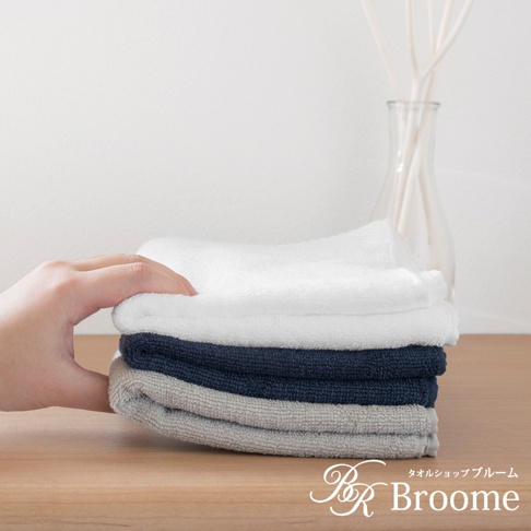 疊放的今治純棉毛巾，包含白色、海軍藍和灰色。毛巾表面有細緻的菱紋質感。