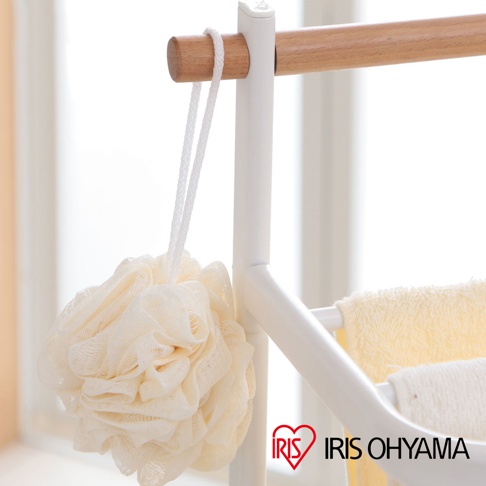 白色金屬框架的毛巾架，搭配原木橫桿，懸掛著一個米白色網狀沐浴球，下方掛有黃色和白色毛巾。