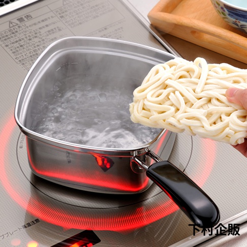 不銹鋼方形單手麵鍋，鍋內裝有沸騰的水，鍋旁有一手正準備放入一塊生麵條。鍋身下方有紅色加熱指示燈。