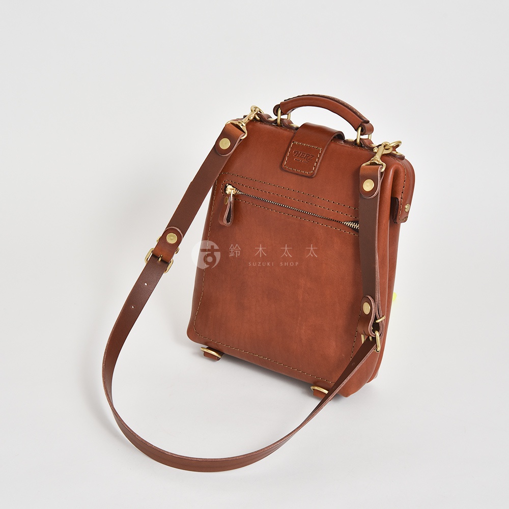 職人手作迷你軟皮杜勒斯包，採用棕色皮革製成，帶有拉鍊前袋、頂部提把和可拆卸肩帶，搭配黃銅色五金配件。