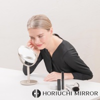 香檳金色桌上型化妝圓鏡，鏡面可旋轉，旁有睫毛膏、粉撲和化妝刷。