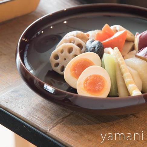 赤飴釉美濃燒圓盤盛有對半切的溏心蛋、蓮藕、竹筍、紅蘿蔔塊及其他食材，盤身呈深棕色，質感光滑。