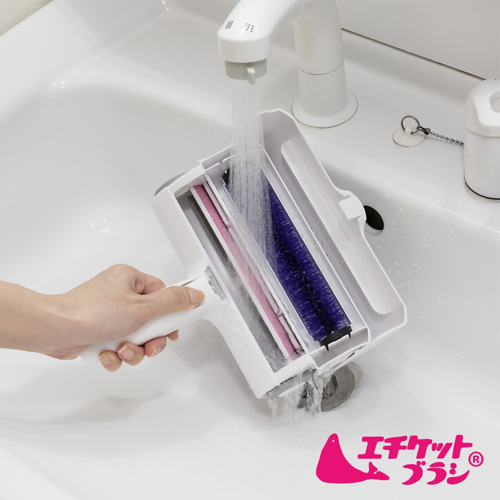 白色雙層除塵滾輪，內含粉色及紫色滾輪，置於白色水槽中，下方有水流通過，左手持握滾輪把手。