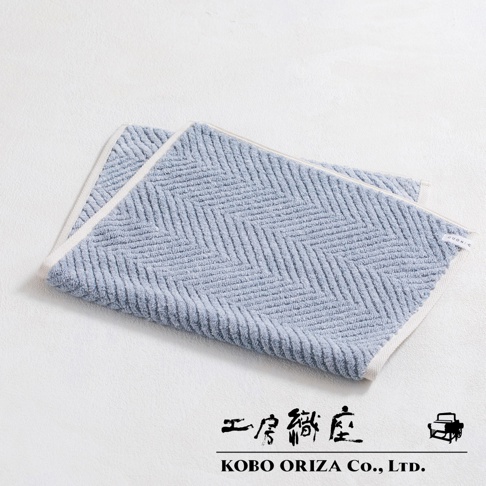 淺藍色棉麻混紡浴墊，織有經典人字紋，邊緣為白色滾邊。