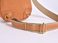 職人手作皮革立體運動斜背包 (F-9) 的特寫，展示了部分淺棕色皮革包身、金屬扣環、登山扣以及由帆布與皮革拼接製成的可調節背帶，背帶上有明顯的縫線和金屬調節扣。