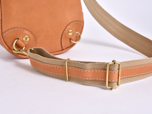 職人手作皮革立體運動斜背包 (F-9) 的特寫，展示了部分淺棕色皮革包身、金屬扣環、登山扣以及由帆布與皮革拼接製成的可調節背帶，背帶上有明顯的縫線和金屬調節扣。