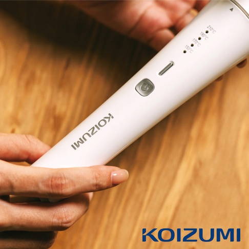 一隻手正拿著一支白色的電捲棒，上面有 KOIZUMI 的品牌標誌和溫度設定指示。