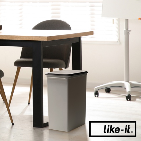 灰色掀蓋式高版垃圾桶，方形設計，搭配黑色細長邊框，置於木質桌面與黑色桌腳的椅子旁。