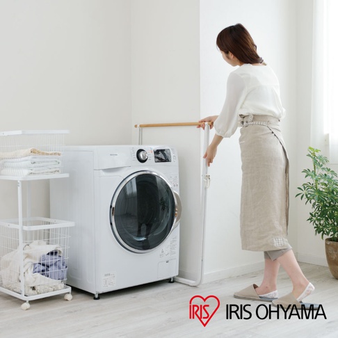 簡約白色金屬框架搭配原木橫桿的曬衣架，旁有滾筒式洗衣機與白色置物架，架上與下方籃筐內有衣物，一位女性穿著亞麻圍裙站在曬衣架旁。