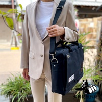 一位身穿米色西裝的女士，左肩斜挎著一個黑色純棉帆布製成的B4公事包，包上配有黑色肩帶及金屬扣環。