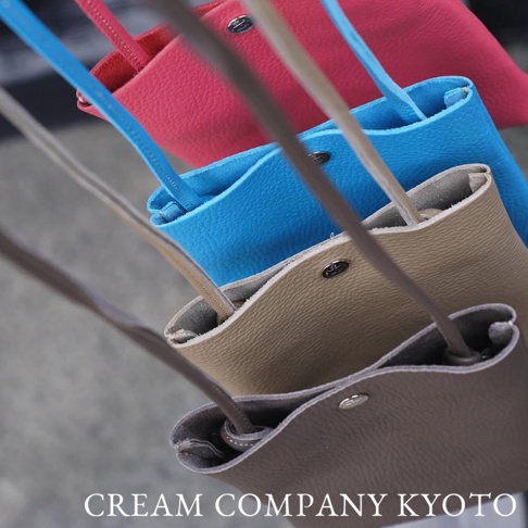 多個京都職人手作隨身手機包，展示了粉紅色、藍色、淺棕色和深棕色。包包由皮革製成，設計簡潔，配有細長的肩帶。