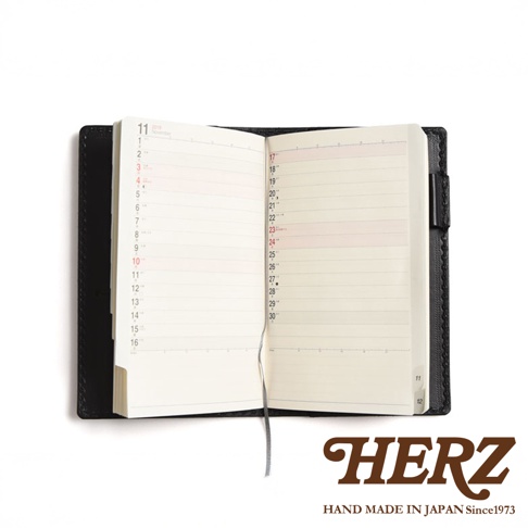 職人手作黑色皮革輕便記事本書套，打開的內頁顯示十一月日曆，內頁為橫線筆記格式，附有書籤帶。