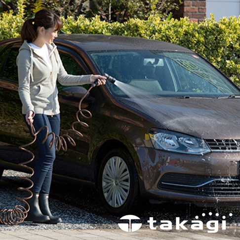 一名女子手持棕色螺旋狀的室外澆花灑水專用水管，正在為一輛深棕色汽車沖洗。