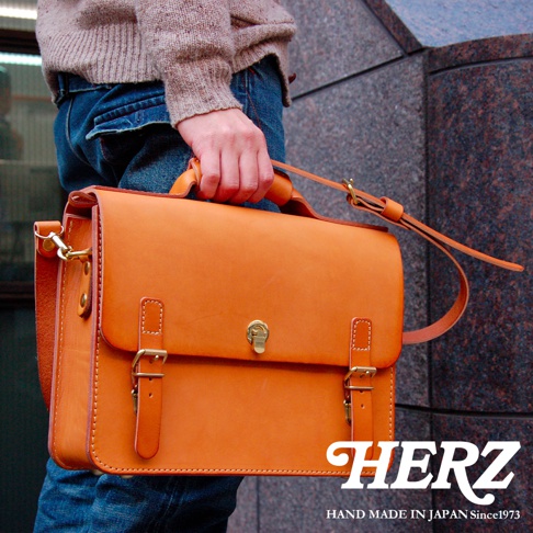 職人手作皮革經典三扣兩用商務公事包，以橙色皮革製成，設有金色扣環和可調節肩帶，適合商務場合使用。