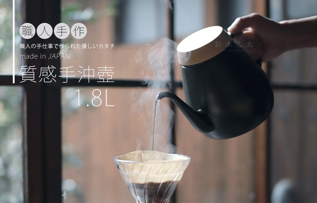 黑色琺瑯手沖壺，配有木質壺蓋，正從細長壺嘴傾倒熱水，水流注入玻璃濾杯中，壺身標有「1.8L」。