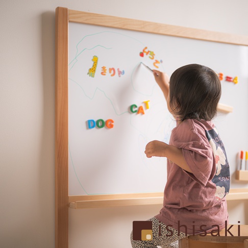 木質邊框的兒童多功能繪畫白板，上面有綠色線條勾勒的圖案，以及彩色磁性字母組成的單詞「DOG」、「CAT」，還有日文「きりん」和「いちご」，以及數字「=4」。一個小孩正在白板上畫畫。